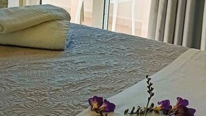 Une chambre d’hôtel avec un lit, une vue sur la mer et un balcon équipé de chaises et d’une plante.