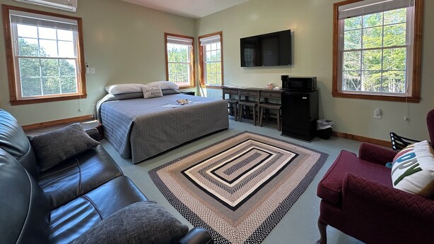 A spacious room with a bed, a desk, a television, and a ceiling fan. - Cozy B&B in walking distance to onsite tasting room in Lee! (Lee)
