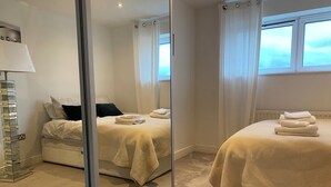A hotel room with a bed, a mirror, a lamp, and a window. - Cosy 2 Bedroom Royal Docks Apartment (London)