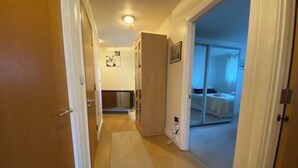 A hallway leading to a bedroom with a bed, a mirror, and a door. - Cosy 2 Bedroom Royal Docks Apartment (London)