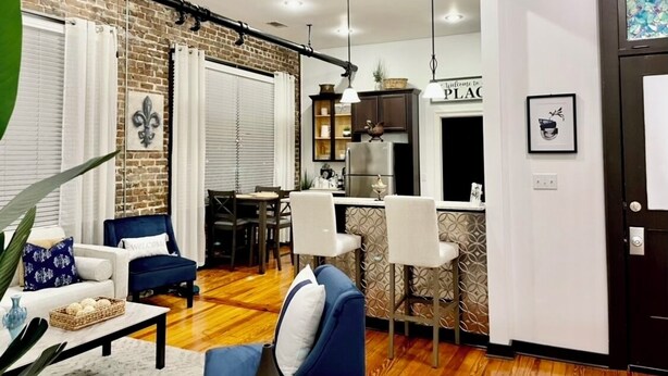 Un salon moderne avec un canapé bleu, une table basse et un coin repas, la cuisine étant visible au fond.