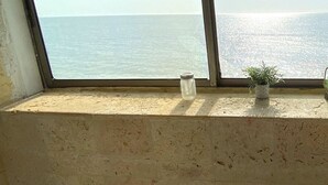 A window with a view of the sea, a small potted plant, and a glass jar on the ledge. - Azul Hotel Boutique (Santa Marta)