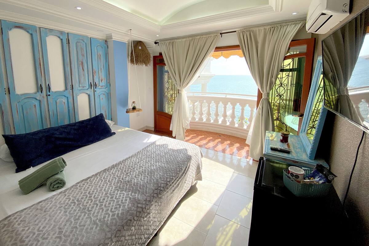 A bedroom with a bed, a view of the sea, and a balcony with a railing.