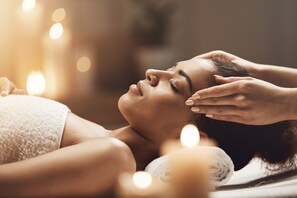 Una persona acostada con las manos en la cabeza, posiblemente recibiendo un masaje, en una habitación con luz tenue y velas.
