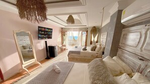 A spacious bedroom with a large bed, a sitting area, a TV, and a view of the sea. - Azul Hotel Boutique (Santa Marta)