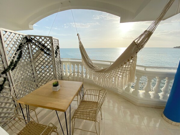 A balcony with a hammock, a table, and chairs, overlooking the sea. - Azul Hotel Boutique (Santa Marta)