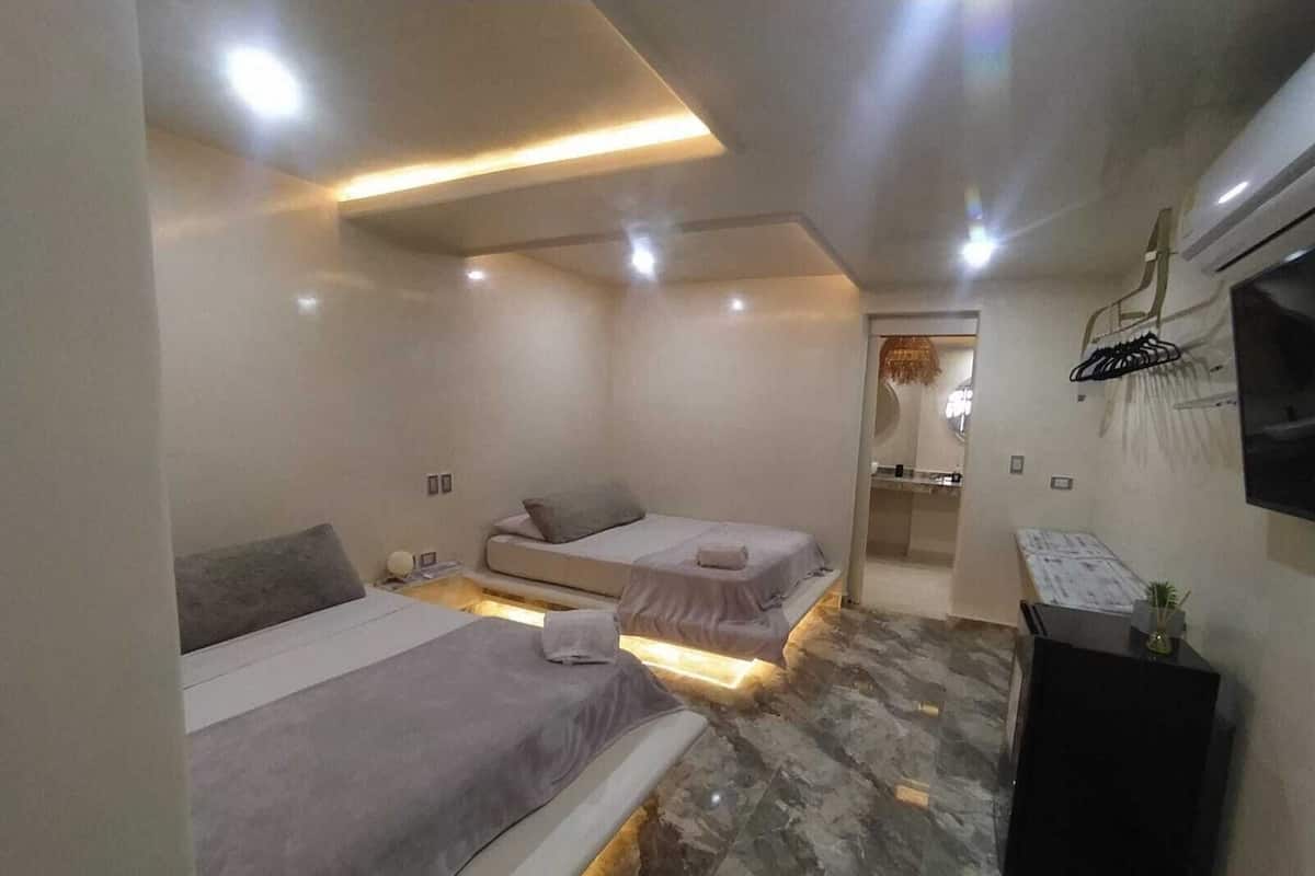 A modern bedroom with two beds, a flat-screen TV, and a small desk.