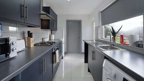 A modern kitchen with dark cabinets, a toaster, a kettle, and a dishwasher. - Comfortable 2BR Home 10 Min to Durham Cathedral (Ushaw Moor)