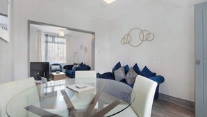 A modern living room with a glass dining table, a sofa with blue cushions, and a wall-mounted circular decoration. - Comfortable 2BR Home 10 Min to Durham Cathedral (Ushaw Moor)