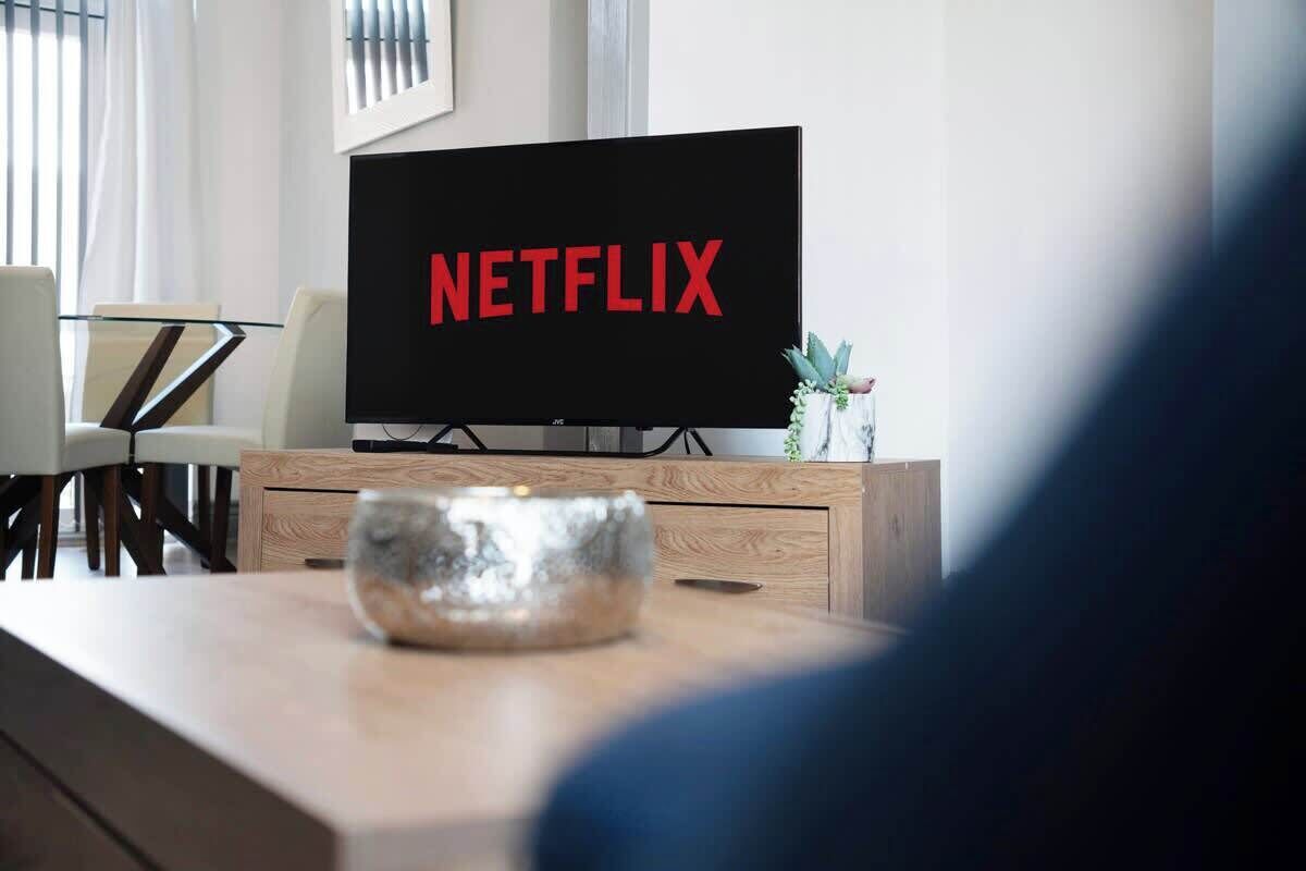 A modern living room with a flat-screen TV displaying the Netflix logo, a wooden coffee table, and a dining area with chairs and a table.