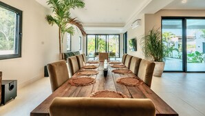 Una larga mesa de comedor con individuales tejidos, sillas acolchadas y una vela en el centro.