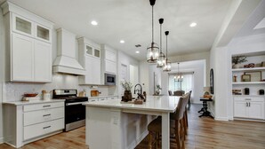 Una cocina amplia con armarios blancos, una isla central y un comedor con sillas de madera.