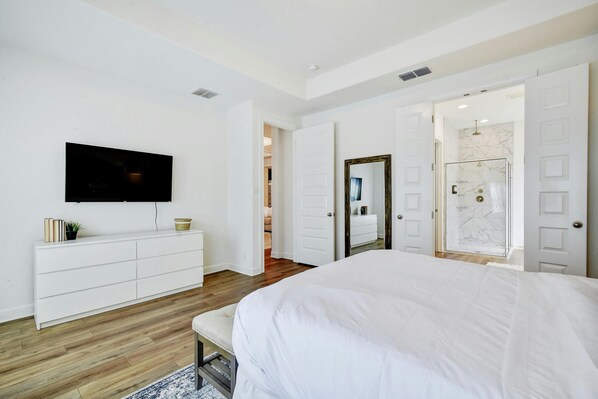 Une chambre avec un grand lit, un téléviseur fixé sur une commode blanche et un dressing doté d’un miroir.