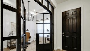 Un interior moderno con un amplio ventanal que da a una habitación, una puerta de madera oscura y una araña.