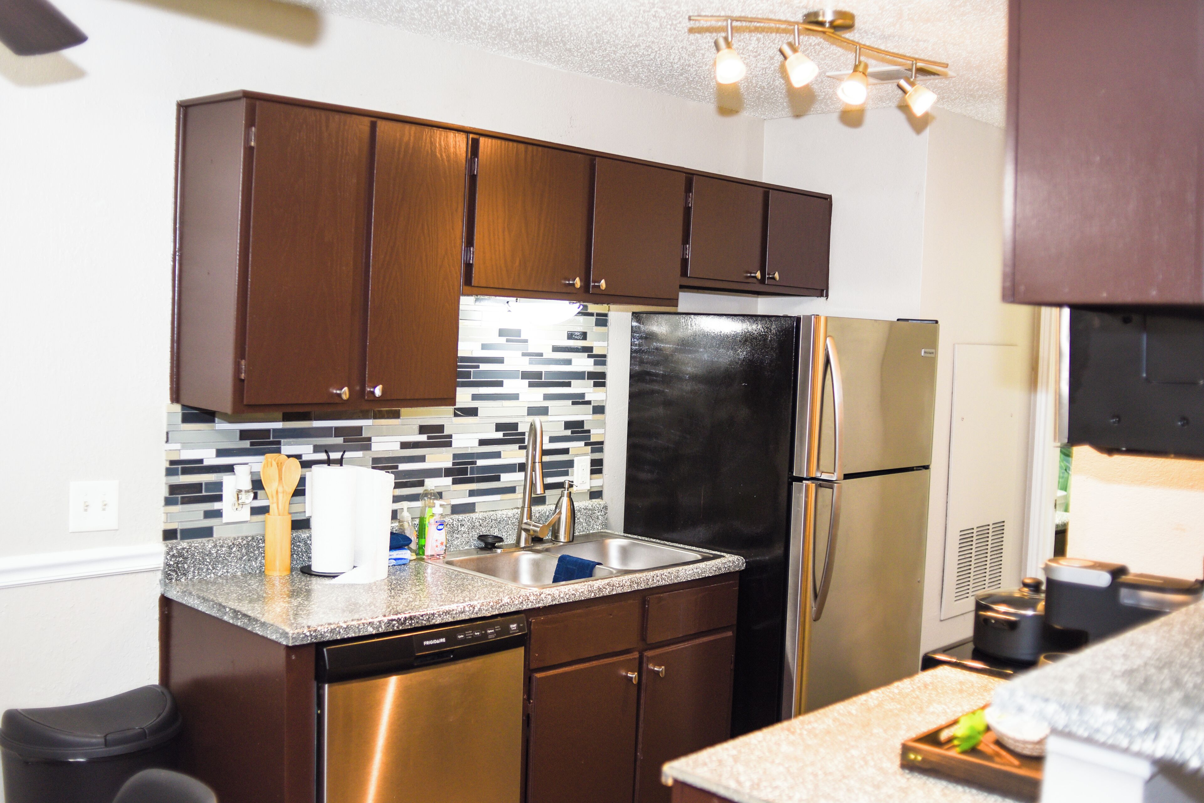 Una cocina moderna con armarios de madera oscura, lavavajillas de acero inoxidable y un refrigerador negro.