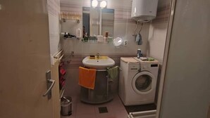 Ein kleines Badezimmer mit Waschbecken, Spiegel und Waschmaschine.