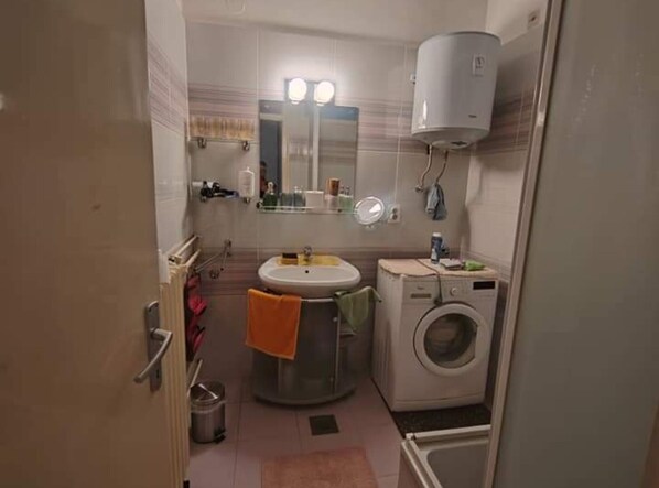 A compact bathroom with a sink, mirror, and a washing machine.