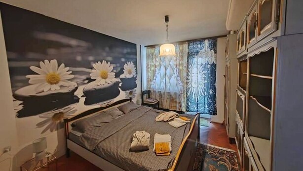 Ein Schlafzimmer mit einem großen Bett, einem Nachttisch, einer Chandelierleuchtre und Blick ins Freie durch ein Fenster mit Vorhängen.