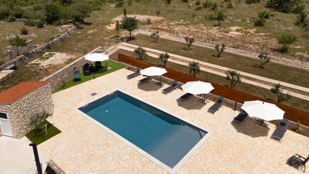 A pool area with lounge chairs and umbrellas, surrounded by a stone wall and a view of a dry landscape with sparse vegetation.