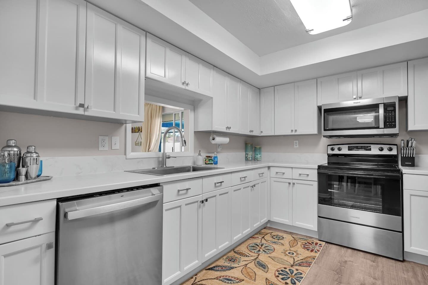 A modern kitchen with white cabinets, stainless steel appliances, a dishwasher, and a patterned rug.