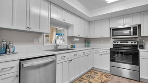 A modern kitchen with white cabinets, stainless steel appliances, a dishwasher, and a patterned rug. - Pool + Ping Pong | Pets OK | Bonita Beach (Bonita Springs)