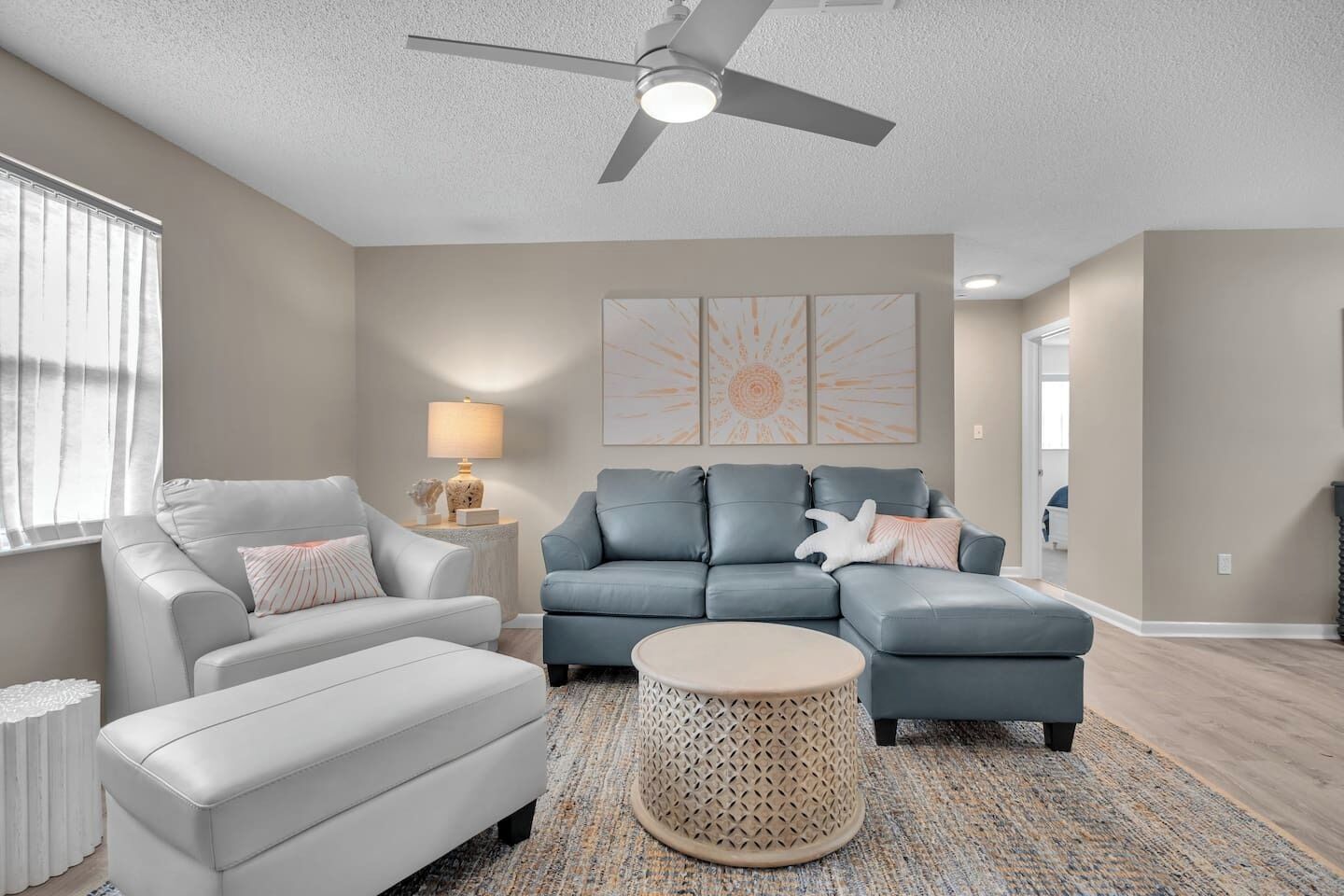 A living room with a grey sectional sofa, a white armchair, a round coffee table, and a ceiling fan.