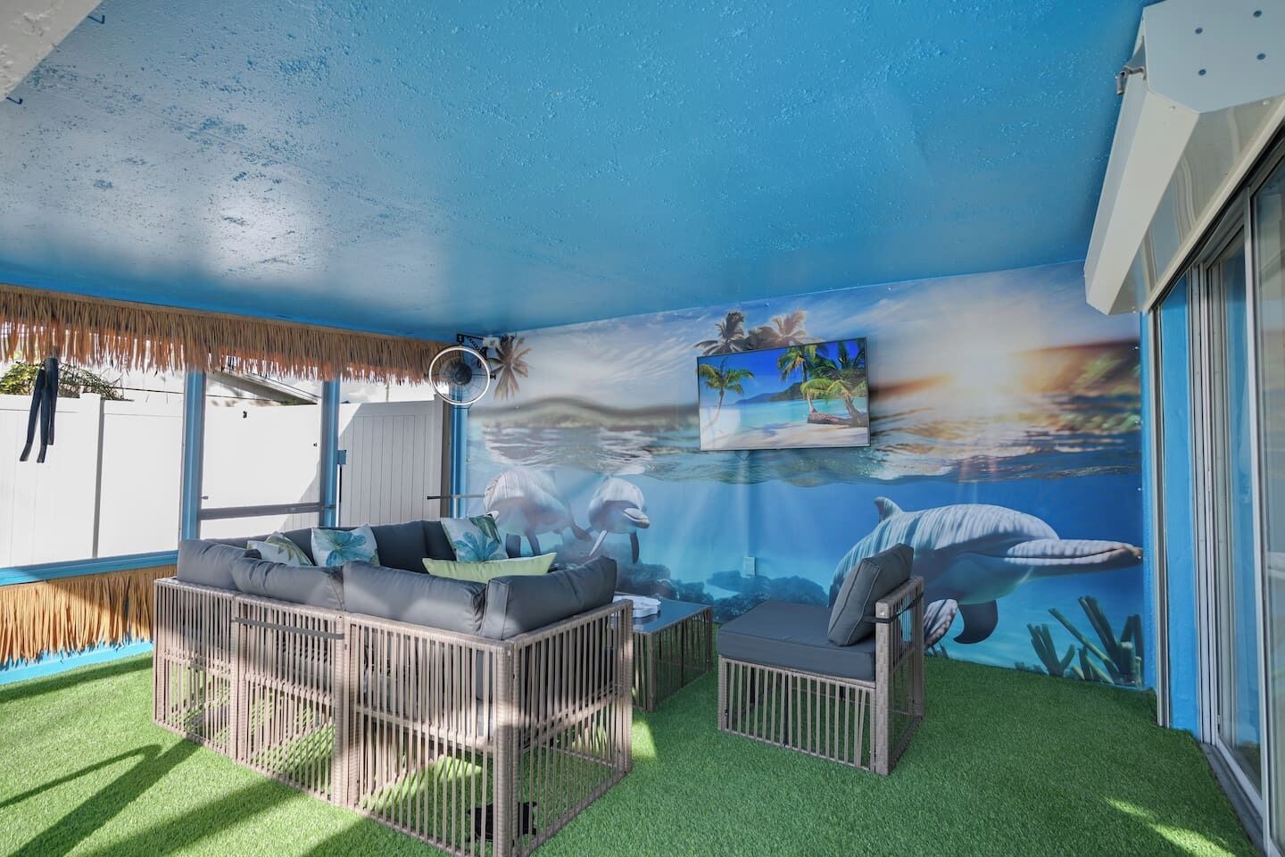 A room with a tropical mural, a sofa, a small table, and a TV.
