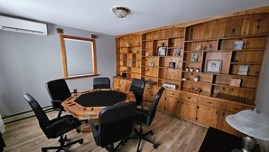 A conference room with a wooden table and chairs, a whiteboard, and a wall with shelves containing framed pictures and small items. - Bayview Hideaway with a great mountains view and large peaceful property. (Whycocomagh)