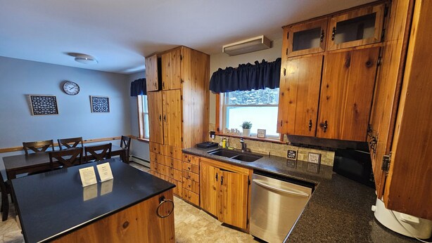 A kitchen with wooden cabinets, a granite countertop, a dishwasher, and a window with curtains. - Bayview Hideaway with a great mountains view and large peaceful property. (Whycocomagh)