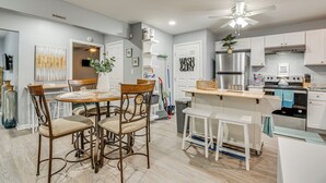 Una cucina moderna con mobili bianchi, un'area pranzo con sedie in legno e una ventola a soffitto.
