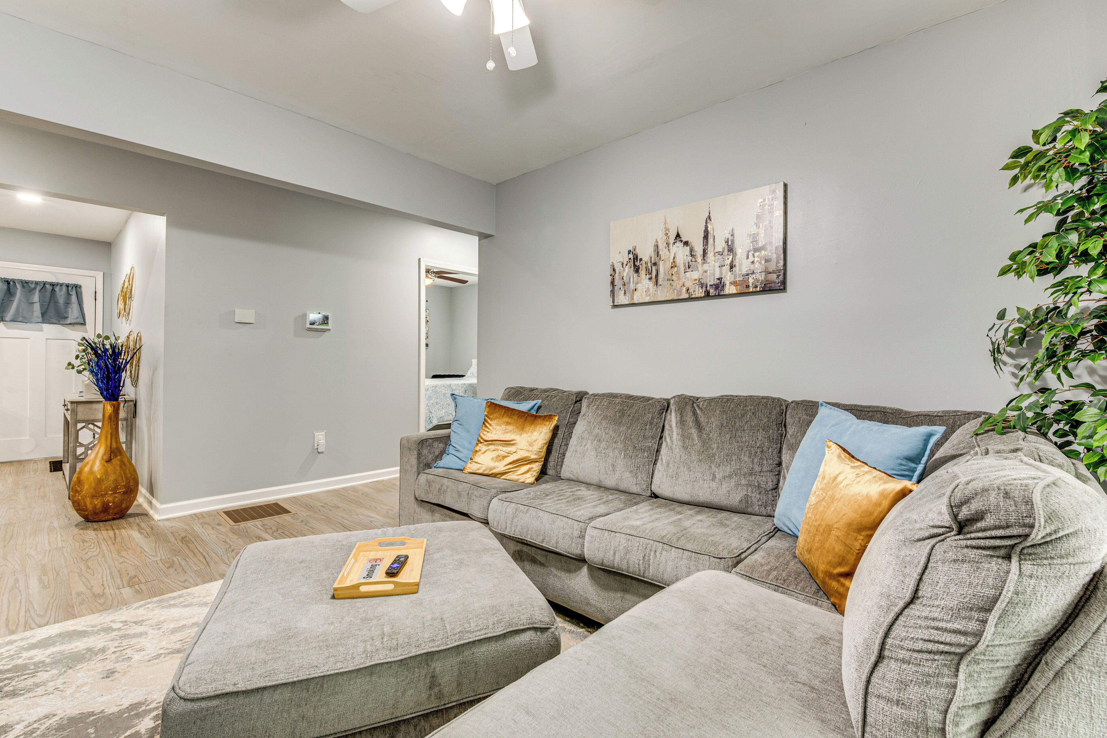 Un salon moderne avec un canapé gris, une table basse et un tableau représentant un paysage urbain accroché au mur.
