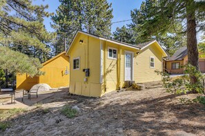 Une maison jaune à deux étages, avec un porche à l’avant, un petit jardin et un arbre devant.
