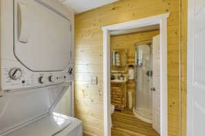 Un espace buanderie comprenant un lave-linge, un mur en bois, ainsi qu’une salle de bain avec douche et toilettes.