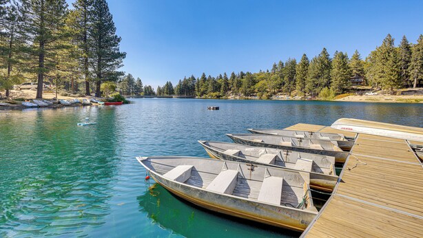 A calm lake with several boats docked at a wooden pier, surrounded by dense forest. - Walk to Water: Cozy Cabin in Green Valley Lake! (Green Valley Lake)