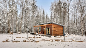 A wooden cabin with a covered porch, surrounded by a snowy forest. - Private Hot Tub: Waterfront Home along Eagle River (Eagle River)