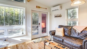 A living room with a leather sofa, a patterned rug, and a large window overlooking a forest. - Private Hot Tub: Waterfront Home along Eagle River (Eagle River)