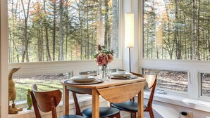 A dining area with a table set for four, large windows offering a view of a forest. - Private Hot Tub: Waterfront Home along Eagle River (Eagle River)