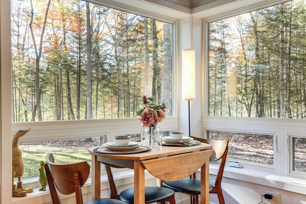 A dining area with a table set for four, large windows offering a view of a forest. - Private Hot Tub: Waterfront Home along Eagle River (Eagle River)