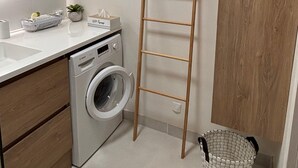 A compact laundry area with a washing machine, a drying rack, a sink, and a small plant.