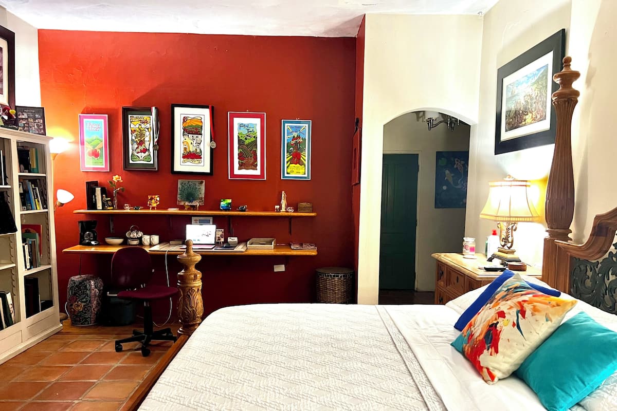Una habitación con cama, escritorio, silla y estanterías con marcos.