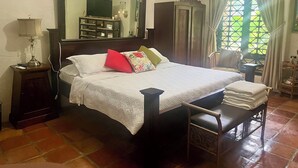 Un dormitorio con cama, mesita de noche con lámpara, silla, armario y ventana con cortinas.