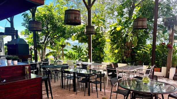 Un patio al aire libre con mesas y sillas redondas, una barra de madera y faroles colgantes.