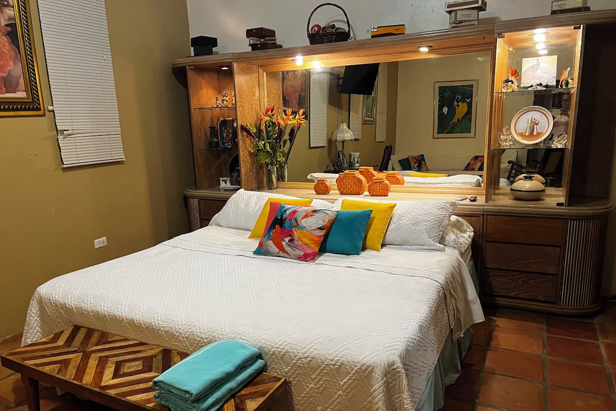 Un dormitorio ordenado con cama, mesitas de noche, un espejo y un banco de madera con toallas.