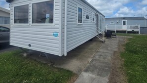 A mobile home with a large window, a porch, and a small deck. - Caravan Kirsty 3 Bedroom (Rhyl)