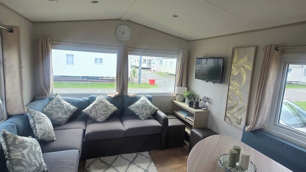 A cozy living area with a sofa set, a coffee table, and a TV mounted on the wall. - Caravan Kirsty 3 Bedroom (Rhyl)
