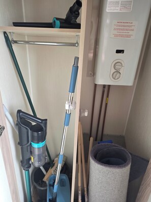 A utility room with a water heater, a vacuum cleaner, a mop, and cleaning tools. - Caravan Paul Sleeps 6 With Free Parking (Rhyl)