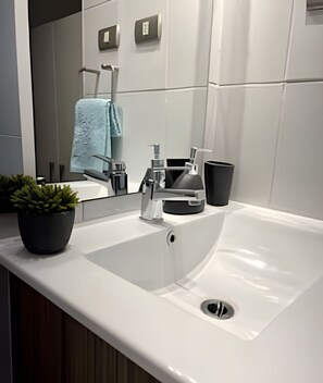 Un baño moderno con un lavamanos blanco, un espejo y una toalla colgada en la pared.