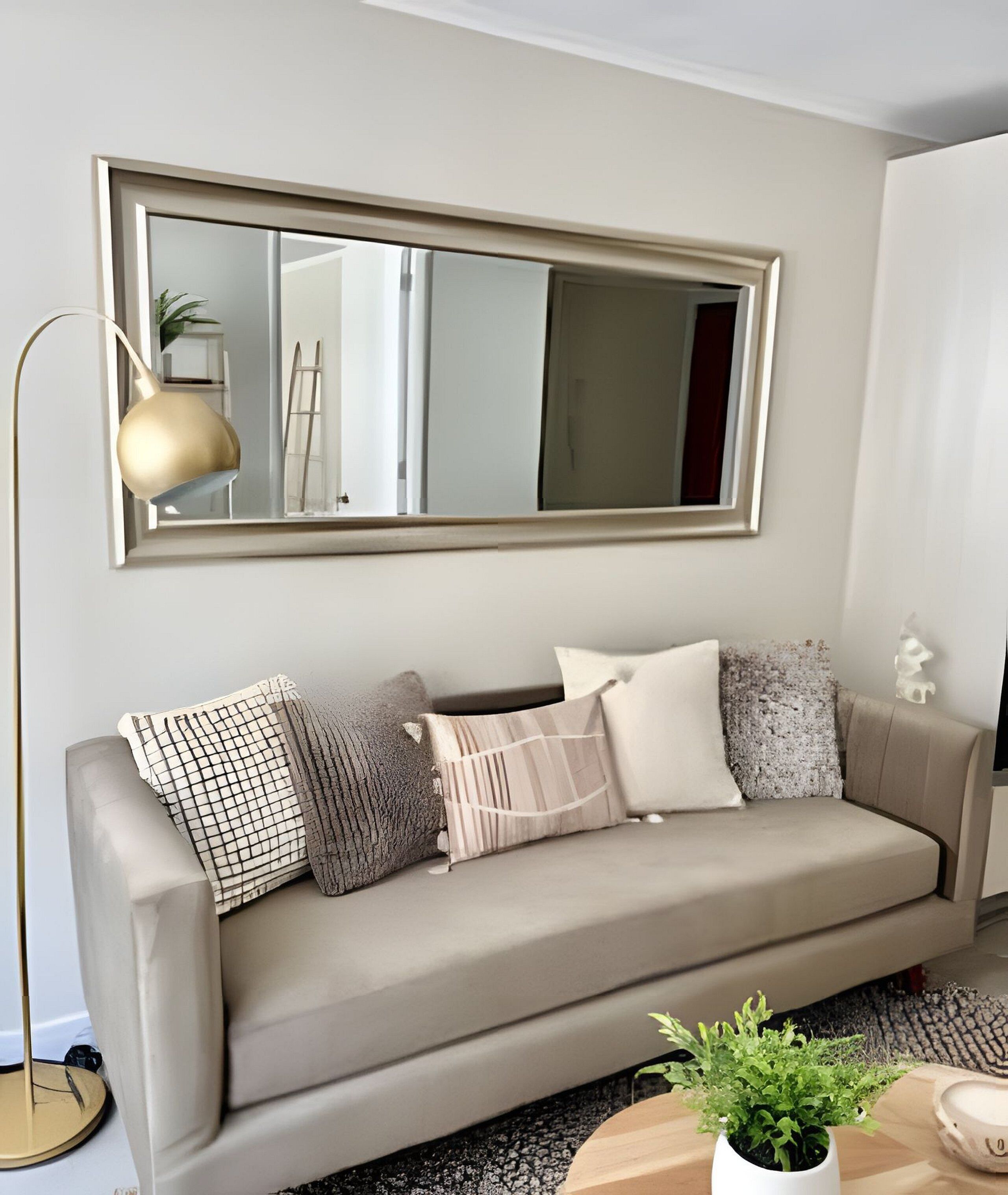 Un salon moderne avec un canapé beige, un grand miroir et une lampe sur pied.