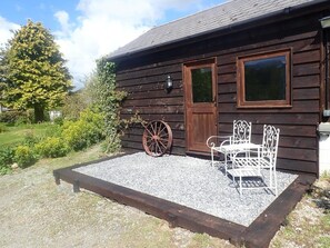 A rustic wooden building with a gravel patio, a metal bench, and a wooden wagon wheel. - Tranquil Lodge Retreat in Penegoes (Machynlleth)