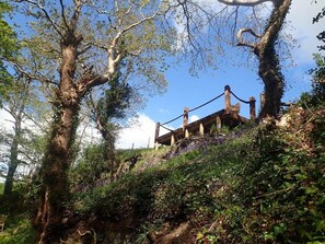 A rustic wooden structure with a sloped roof, surrounded by dense greenery and trees. - Welsh Countryside Retreat - Felin Crewi Cottages (Machynlleth)